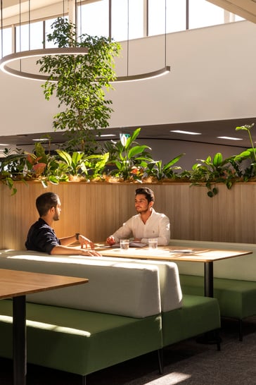 Two people sat in a booth chatting surrounded by greenery. 