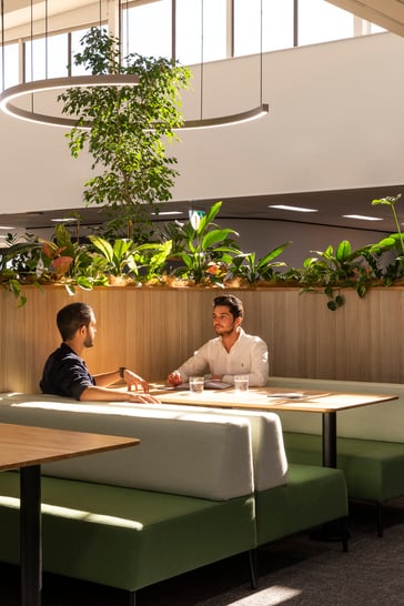 Two people sat in a booth chatting surrounded by greenery.
