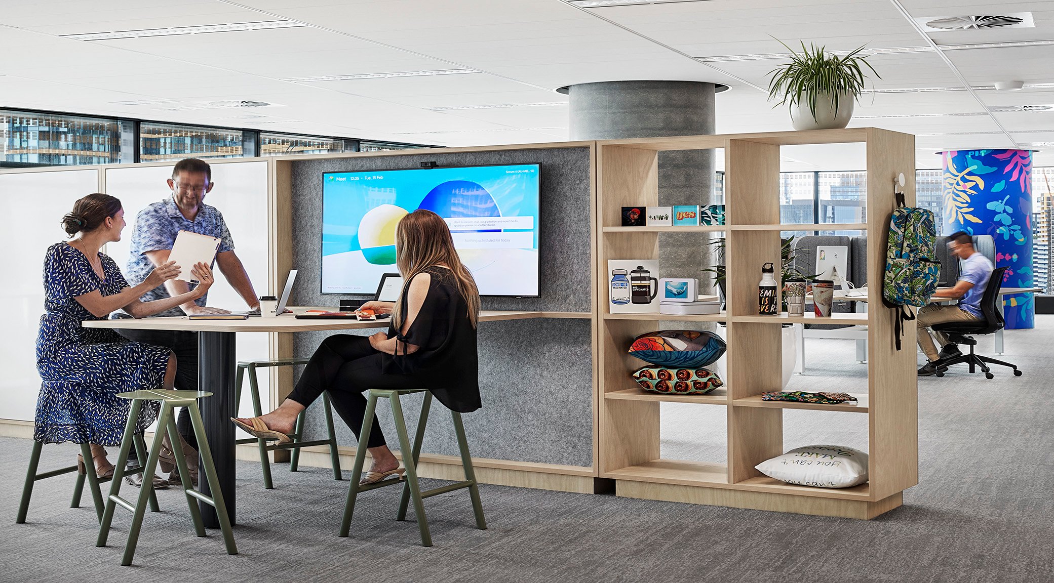 Three people surrounding a breakout area near a TV screen