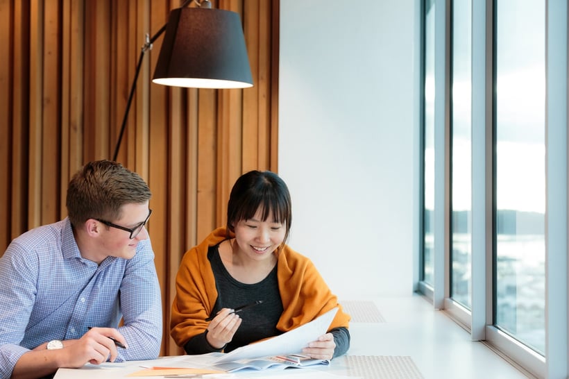 A man and woman collaborating at a table next to the window